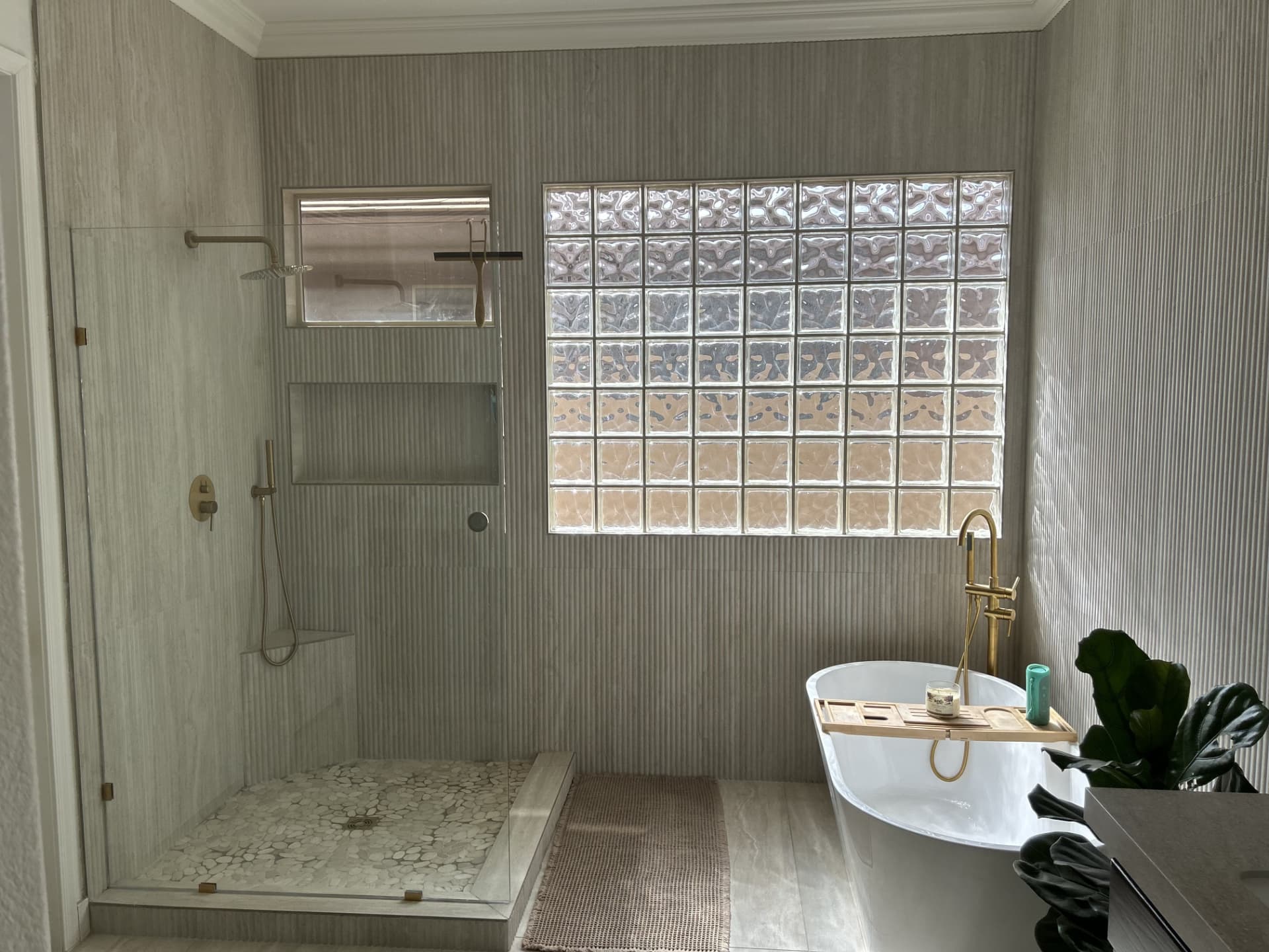 Walk-in shower with pebble floor and freestanding tub beside a glass-block window