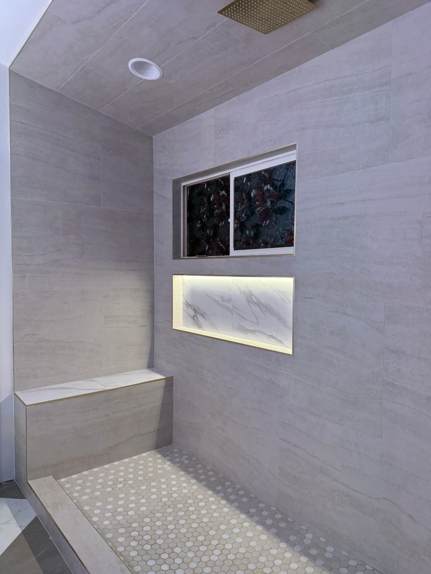 Walk-in shower with hex tile floor, marble bench, and lit niche