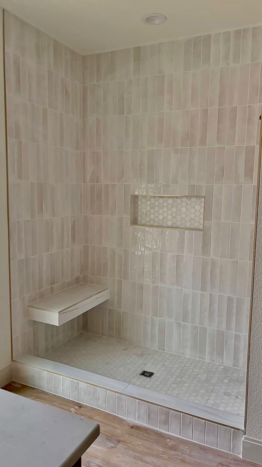 Modern walk-in shower with vertical cream tiles, hex floor, and gold trim