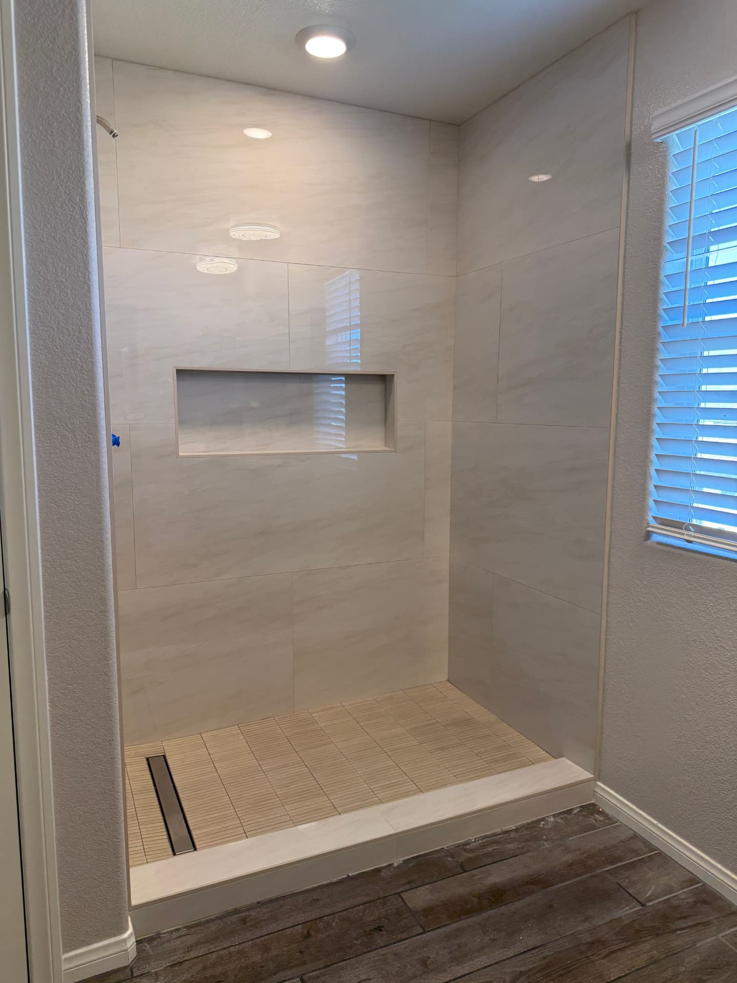 Walk-in shower with large marble wall tiles, linear drain, and white curb
